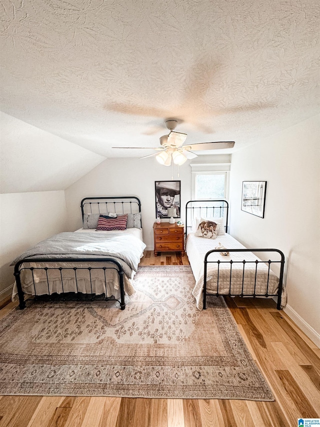 bedroom featuring a textured ceiling, vaulted ceiling, ceiling fan, and hardwood / wood-style flooring