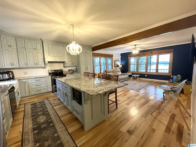 kitchen featuring a kitchen island, decorative light fixtures, a breakfast bar area, light stone counters, and black appliances