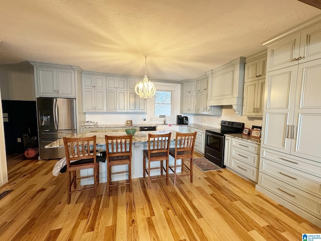 kitchen featuring a kitchen island, decorative light fixtures, black appliances, a textured ceiling, and light wood-type flooring