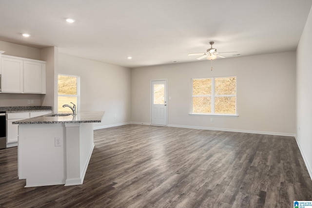 kitchen with sink, dark stone counters, an island with sink, and white cabinets