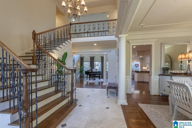 entryway with crown molding, a chandelier, decorative columns, and a high ceiling