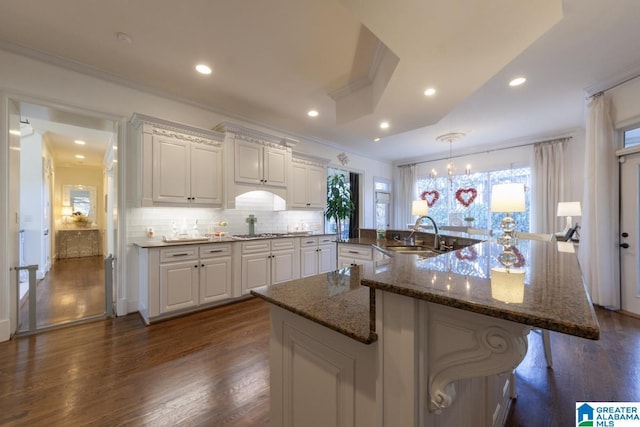 kitchen featuring sink, white cabinetry, dark hardwood / wood-style floors, tasteful backsplash, and a kitchen bar