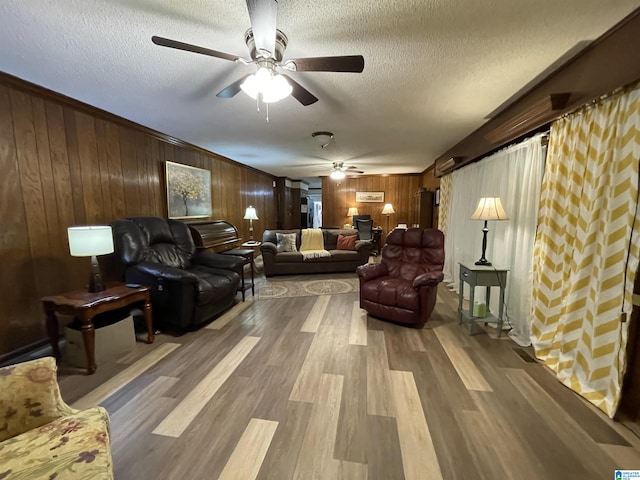 living room featuring ceiling fan, hardwood / wood-style flooring, a textured ceiling, and wood walls