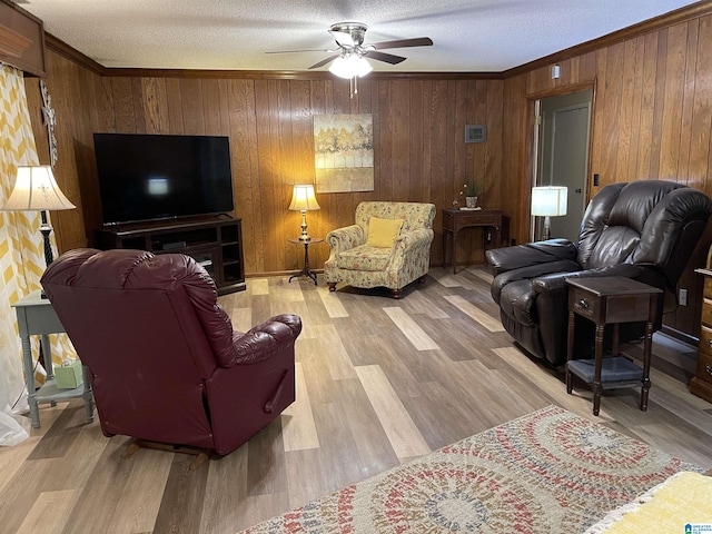 living room with ceiling fan, wooden walls, light hardwood / wood-style floors, and a textured ceiling