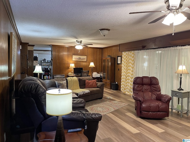 living room with ceiling fan, light wood-type flooring, a textured ceiling, and wood walls