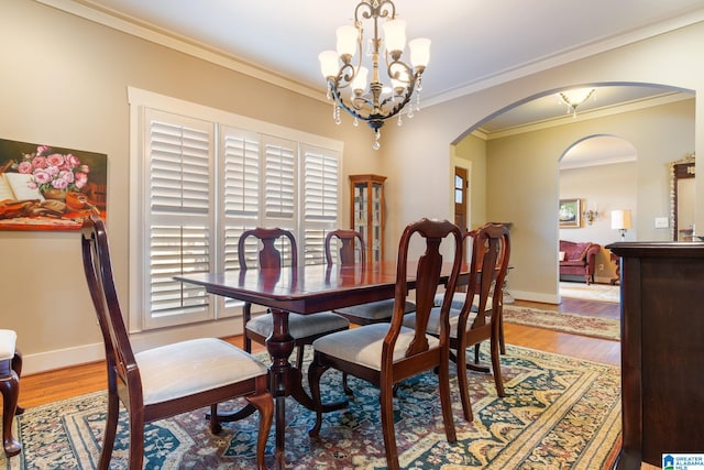 dining space with wood-type flooring, ornamental molding, and a notable chandelier