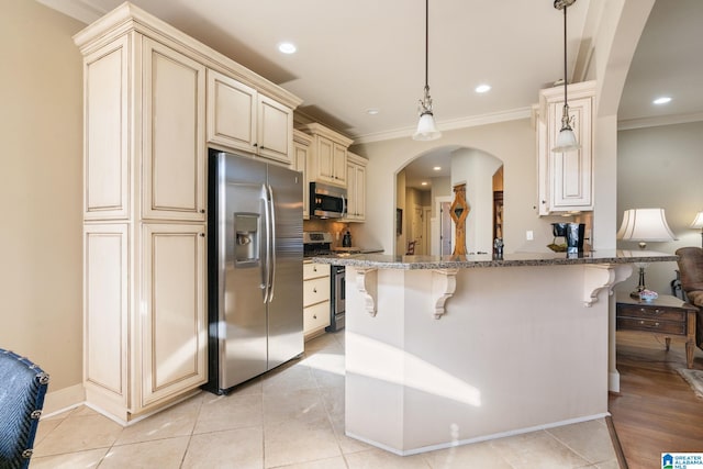 kitchen featuring a kitchen bar, dark stone countertops, appliances with stainless steel finishes, pendant lighting, and cream cabinets