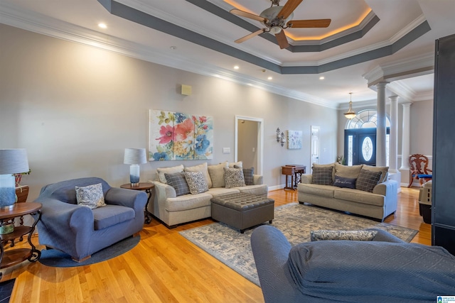 living room featuring light hardwood / wood-style floors, ornamental molding, a raised ceiling, and decorative columns