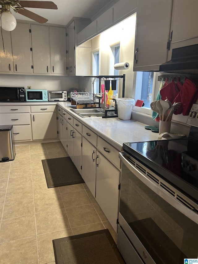 kitchen featuring light tile patterned flooring, stainless steel range with electric stovetop, ceiling fan, and sink