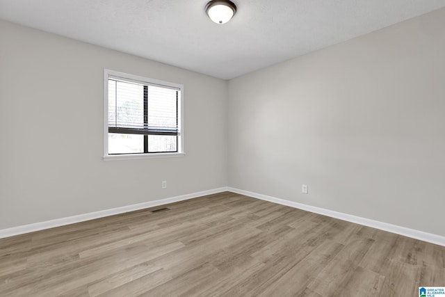 empty room with light wood finished floors, baseboards, visible vents, and a textured ceiling