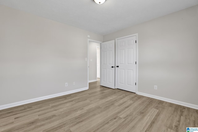 unfurnished bedroom featuring light wood-type flooring, a closet, and baseboards