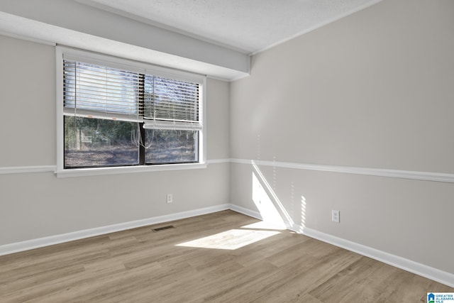 spare room featuring visible vents, a textured ceiling, baseboards, and wood finished floors