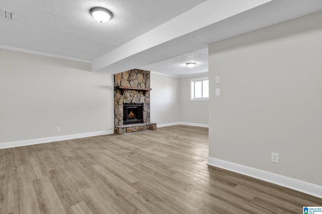 unfurnished living room with visible vents, wood finished floors, a stone fireplace, crown molding, and a textured ceiling