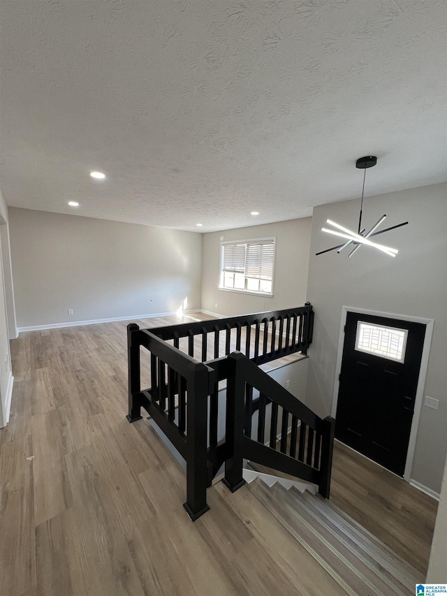 interior space with a textured ceiling, a chandelier, wood finished floors, and baseboards