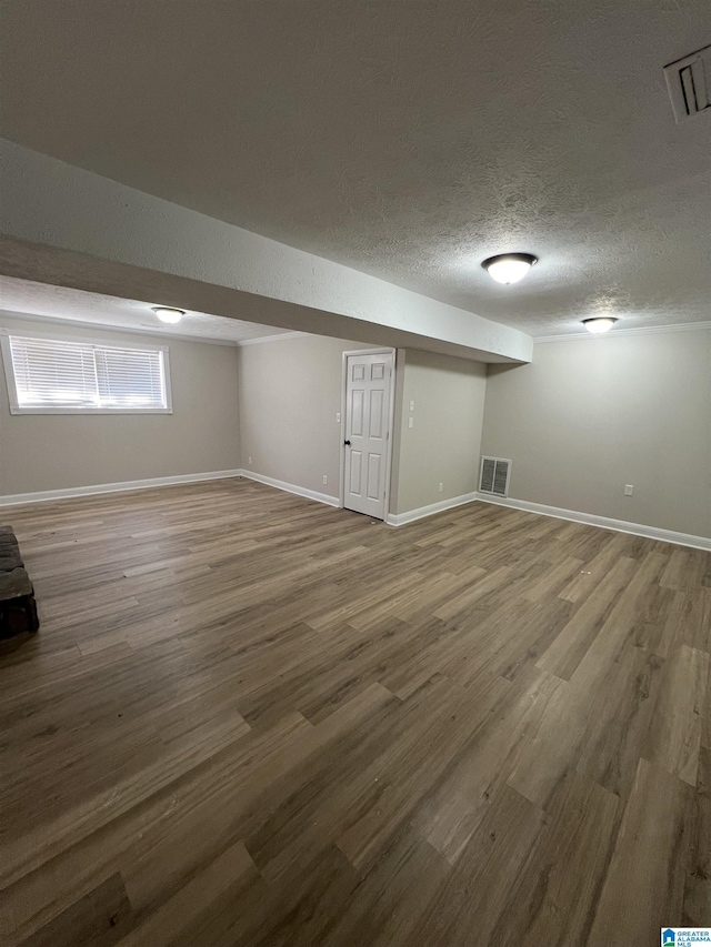 basement with a textured ceiling, wood finished floors, visible vents, and baseboards