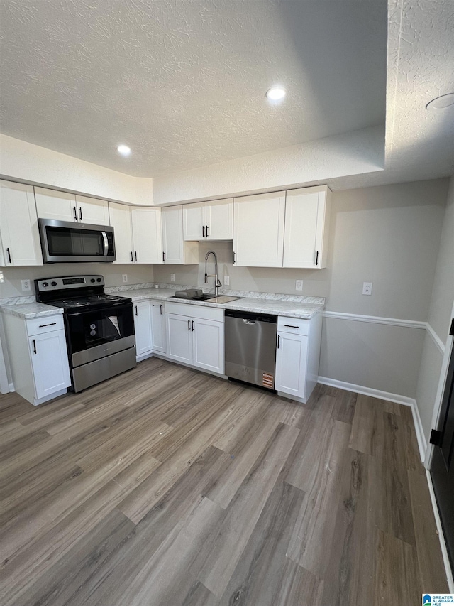 kitchen with stainless steel appliances, light wood-style floors, a sink, and white cabinets