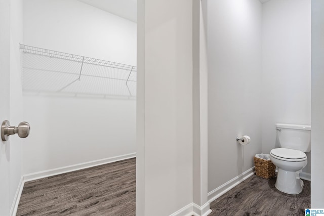 bathroom with toilet, baseboards, a walk in closet, and wood finished floors