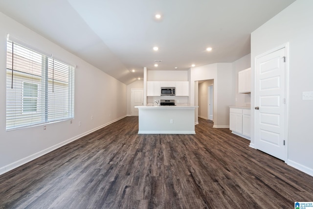 kitchen with lofted ceiling, dark wood-type flooring, white cabinetry, stainless steel appliances, and a center island with sink