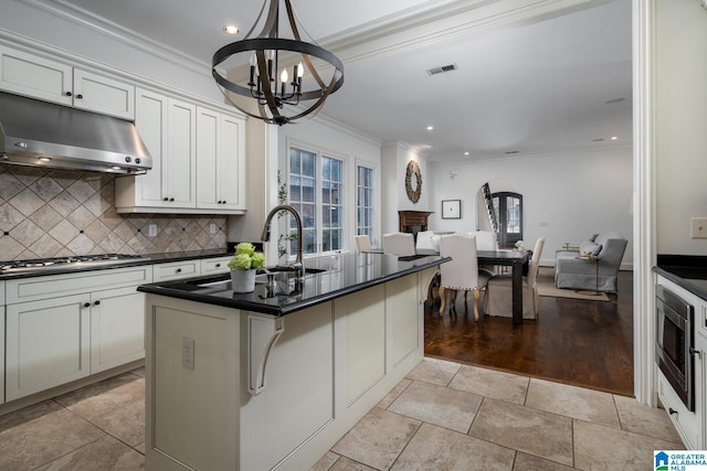 kitchen with backsplash, a notable chandelier, a kitchen island with sink, and white cabinets