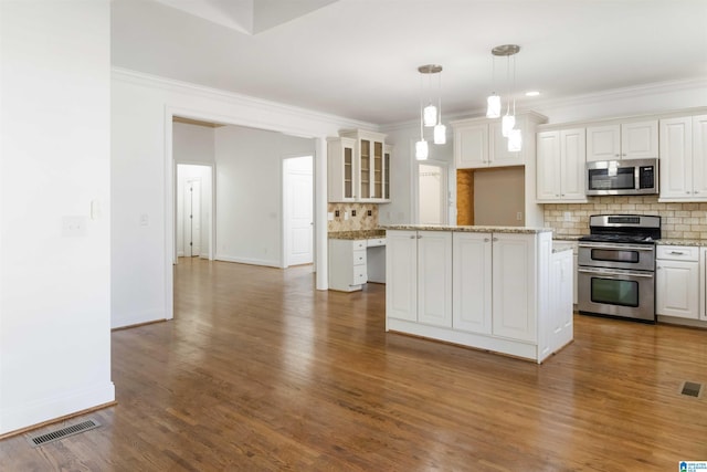 kitchen featuring stainless steel appliances, a center island, ornamental molding, white cabinets, and decorative light fixtures