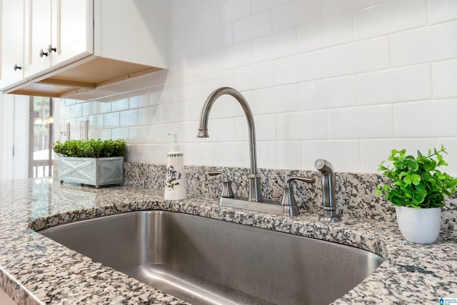 room details featuring light stone countertops, sink, white cabinets, and decorative backsplash