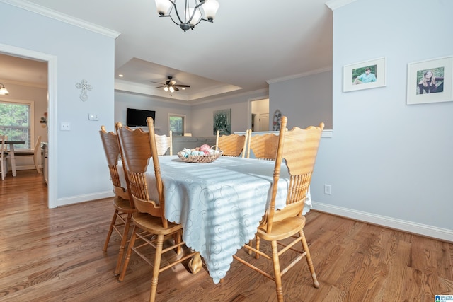 dining room with ornamental molding, wood-type flooring, a tray ceiling, and ceiling fan with notable chandelier