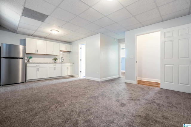 unfurnished living room featuring sink, carpet, and a drop ceiling