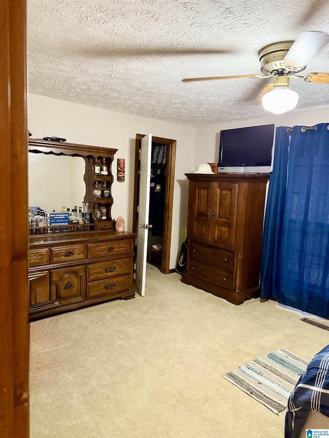 bedroom with ceiling fan, light colored carpet, and a textured ceiling