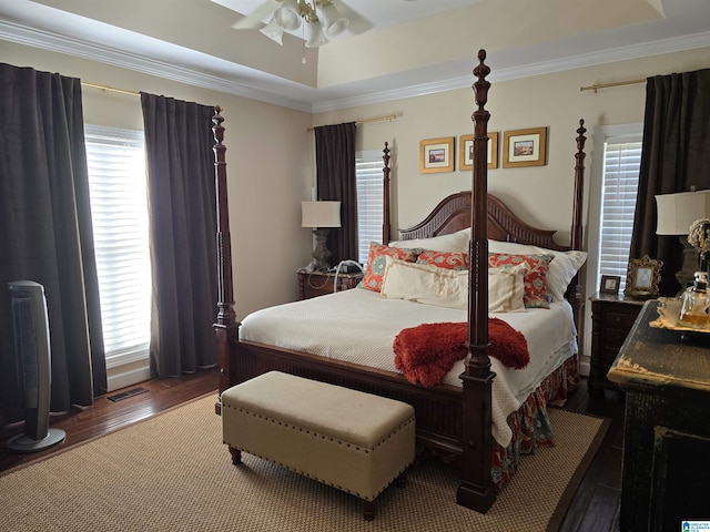 bedroom with hardwood / wood-style flooring, ceiling fan, a raised ceiling, and multiple windows