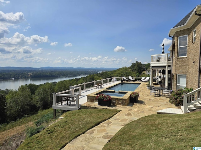 view of swimming pool featuring a water view, a patio, an in ground hot tub, and a lawn