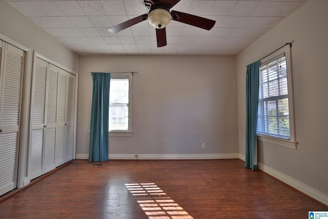 unfurnished bedroom featuring multiple windows, dark hardwood / wood-style flooring, two closets, and ceiling fan