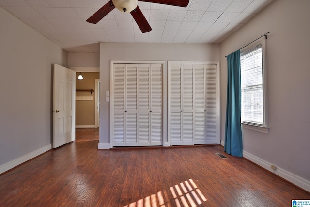 unfurnished bedroom with dark hardwood / wood-style flooring, two closets, and ceiling fan