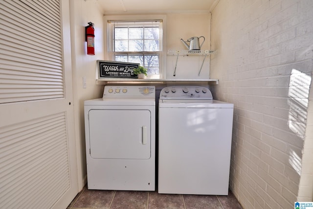 laundry area featuring crown molding, washer and clothes dryer, dark tile patterned floors, and brick wall