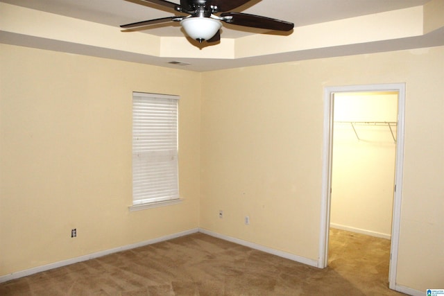 unfurnished bedroom featuring a spacious closet, light carpet, a tray ceiling, a closet, and ceiling fan