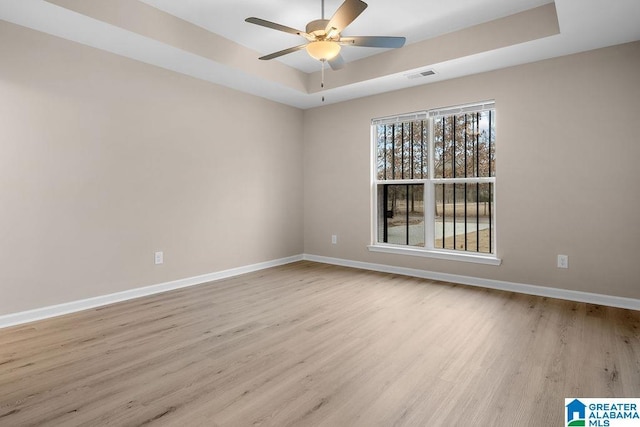 empty room featuring a raised ceiling, ceiling fan, and light wood-type flooring