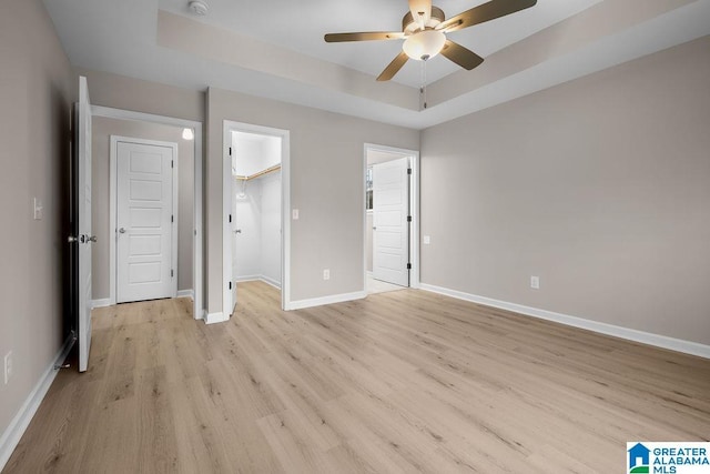 unfurnished bedroom with ceiling fan, a tray ceiling, light hardwood / wood-style floors, and a spacious closet