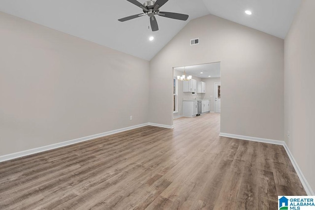 unfurnished living room with high vaulted ceiling, ceiling fan with notable chandelier, and light wood-type flooring