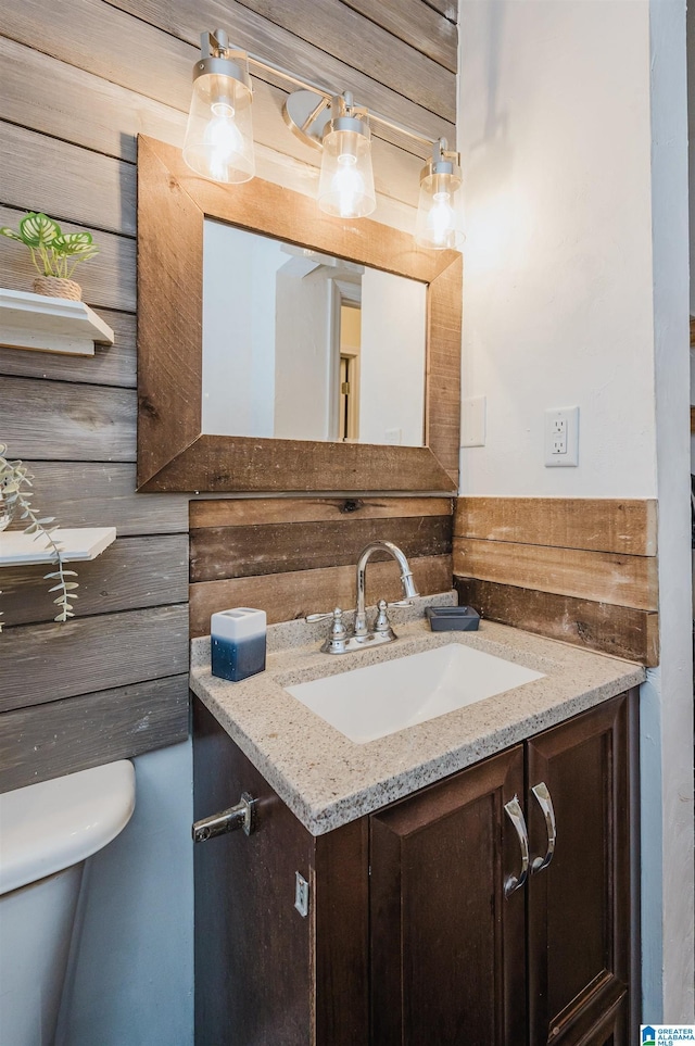 bathroom with vanity, wooden walls, and toilet