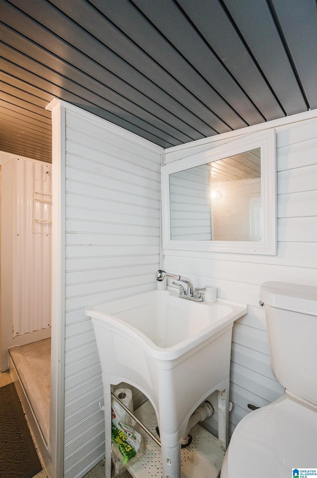 bathroom featuring wood ceiling, toilet, sink, and wood walls