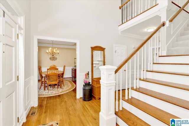 foyer entrance featuring crown molding, a towering ceiling, an inviting chandelier, and light wood-type flooring