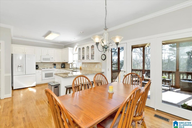 dining space featuring crown molding, sink, a notable chandelier, and light hardwood / wood-style flooring