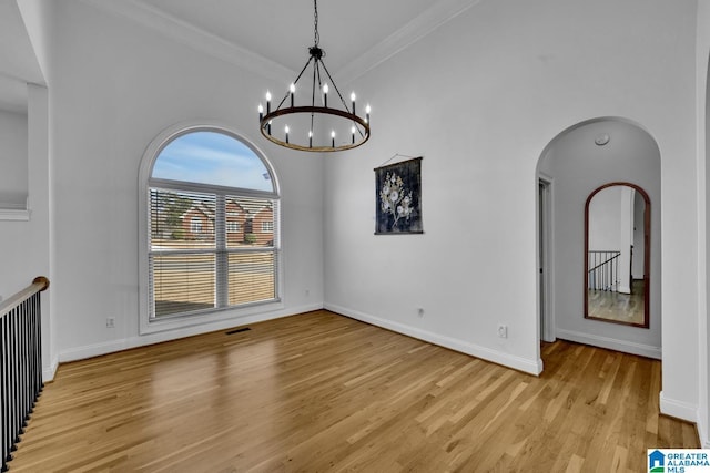 unfurnished dining area featuring a high ceiling, ornamental molding, a notable chandelier, and light hardwood / wood-style floors