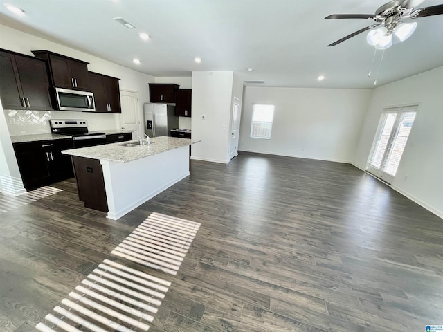 kitchen with dark wood-type flooring, sink, tasteful backsplash, appliances with stainless steel finishes, and an island with sink