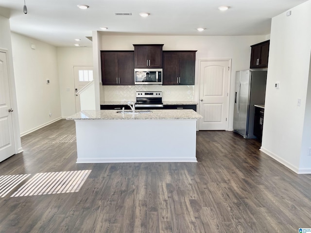 kitchen with tasteful backsplash, dark brown cabinets, an island with sink, stainless steel appliances, and light stone countertops