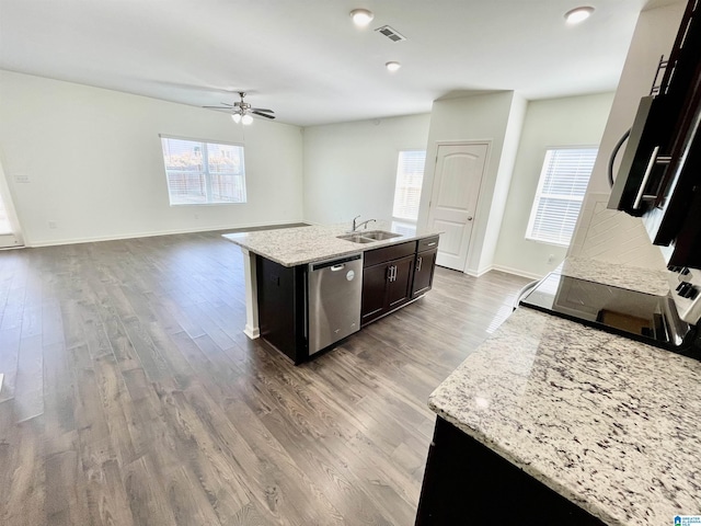 kitchen with stainless steel appliances, light stone countertops, an island with sink, and plenty of natural light