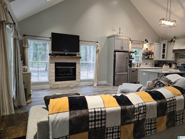 interior space with high vaulted ceiling, a fireplace, baseboards, and wood finished floors