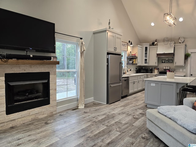 kitchen with decorative light fixtures, a kitchen island, light countertops, appliances with stainless steel finishes, and glass insert cabinets