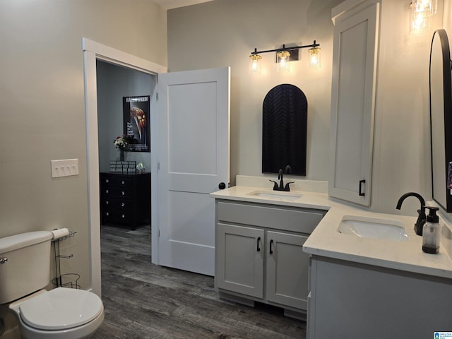 full bath featuring double vanity, toilet, a sink, and wood finished floors