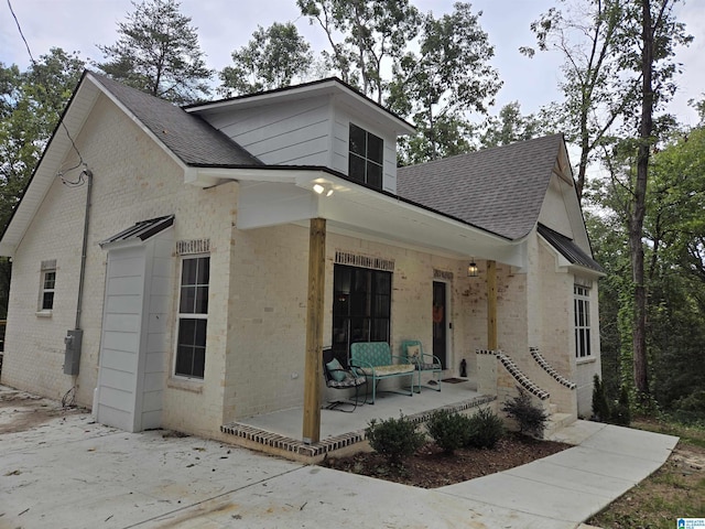 view of front of home with a shingled roof, a patio area, and brick siding