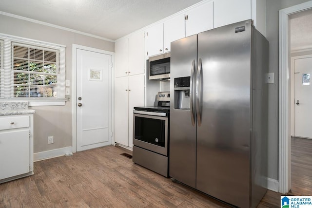 kitchen with ornamental molding, stainless steel appliances, light hardwood / wood-style flooring, and white cabinets